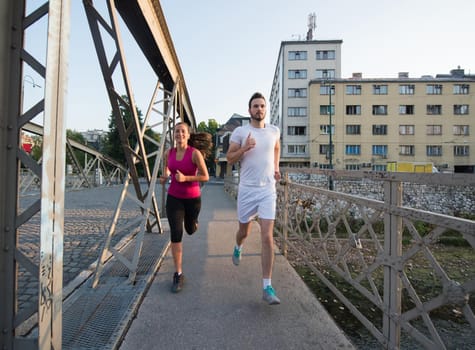 urban sports, healthy young couple jogging across the bridge in the city at sunny morning