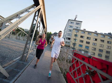 urban sports, healthy young couple jogging across the bridge in the city at sunny morning