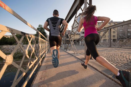 urban sports, healthy young couple jogging across the bridge in the city at sunny morning