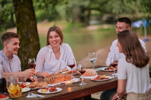 group of happy friends having picnic french dinner party outdoor during summer holiday vacation near the river at beautiful nature