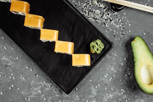 Traditional fresh japanese sushi rolls on a black stone Teka Kaji. Roll ingredients: cheese cheder, philadelphia cheese, cucumber, tuna chips, nori, rice.