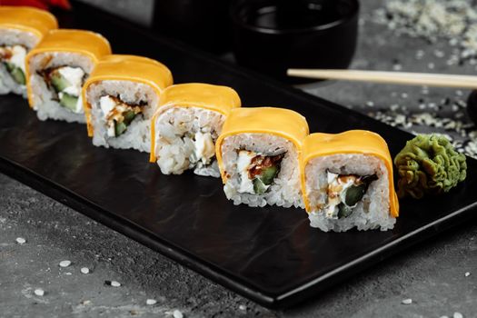 Traditional fresh japanese sushi rolls on a black stone Teka Kaji. Roll ingredients: cheese cheder, philadelphia cheese, cucumber, tuna chips, nori, rice.