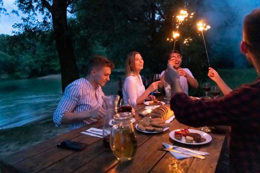 group of happy friends having picnic french dinner party outdoor during summer holiday vacation near the river at beautiful nature