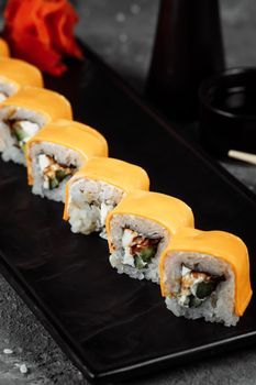 Traditional fresh japanese sushi rolls on a black stone Teka Kaji. Roll ingredients: cheese cheder, philadelphia cheese, cucumber, tuna chips, nori, rice.