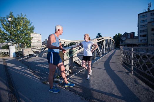 jogging couple check music playlist on phone and plan route before morning running workout  with sunrise in the city  and sun flare in background