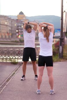 jogging couple warming up and stretching before morning running in the city