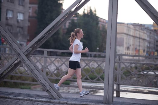 sporty woman running on sidewalk at early morning with city  sunrise scene in background