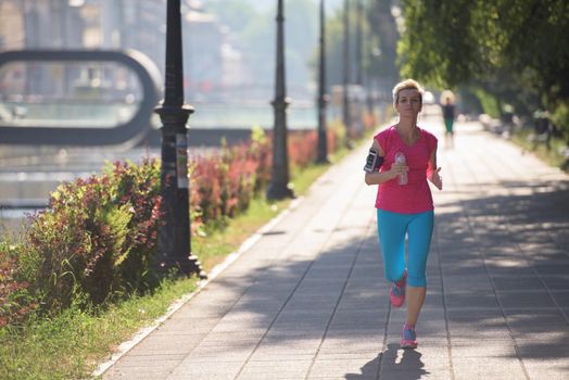 sporty woman running on sidewalk at early morning with city  sunrise scene in background