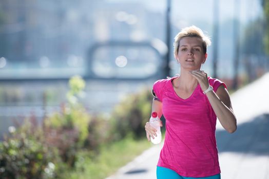 sporty woman running on sidewalk at early morning with city  sunrise scene in background