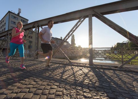 healthy mature couple jogging in the city  at early morning with sunrise in background