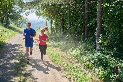 young happy couple enjoying in a healthy lifestyle while jogging on a country road through the beautiful sunny forest, exercise and fitness concept