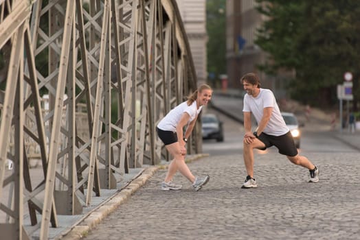 jogging couple warming up and stretching before morning running training workout  in the city with sunrise in background