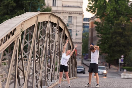 jogging couple warming up and stretching before morning running training workout  in the city with sunrise in background