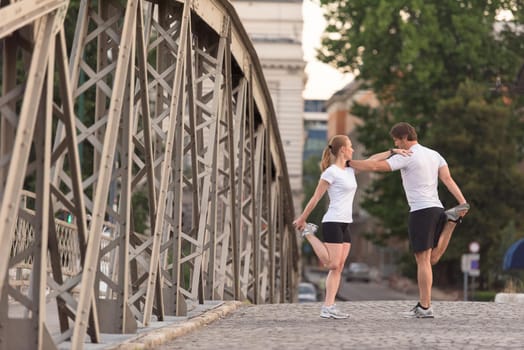 jogging couple warming up and stretching before morning running training workout  in the city with sunrise in background