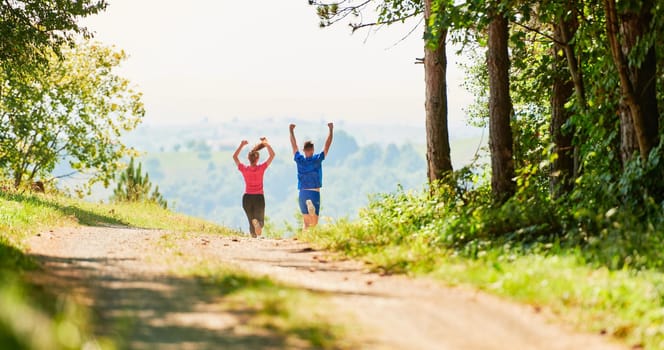 young happy couple enjoying in a healthy lifestyle while jogging on a country road through the beautiful sunny forest, exercise and fitness concept