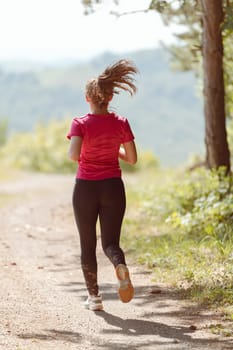 woman enjoying in a healthy lifestyle while jogging on a country road through the beautiful sunny forest, exercise and fitness concept