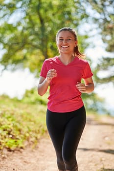 woman enjoying in a healthy lifestyle while jogging on a country road through the beautiful sunny forest, exercise and fitness concept