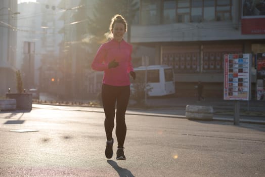 sporty woman running on sidewalk at early morning jogging with city  sunrise scene in background