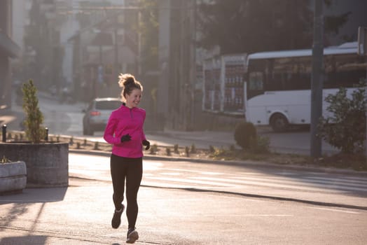 sporty woman running on sidewalk at early morning jogging with city  sunrise scene in background