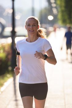 sporty woman running on sidewalk at early morning with city  sunrise scene in background