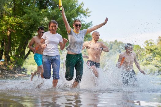 Summer joy group of happy friends having fun while running and splashing on river