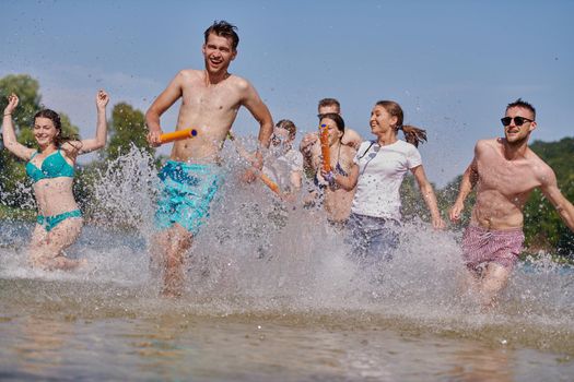 Summer joy group of happy friends having fun while running and splashing on river