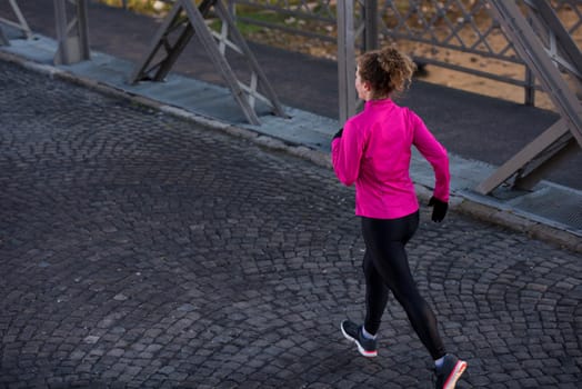 sporty woman running on sidewalk at early morning jogging with city  sunrise scene in background