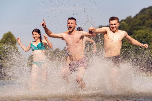 Summer joy group of happy friends having fun while running and splashing on river