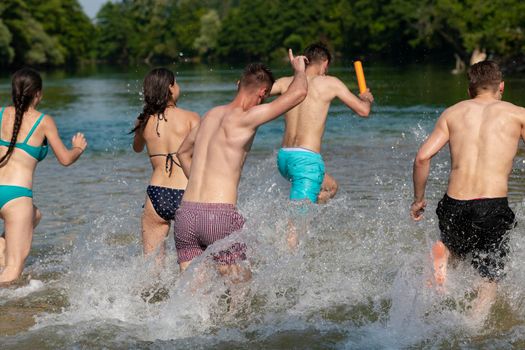 Summer joy group of happy friends having fun while running and splashing on river