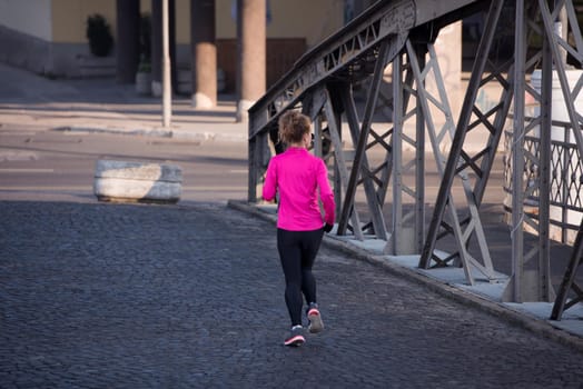 sporty woman running on sidewalk at early morning jogging with city  sunrise scene in background