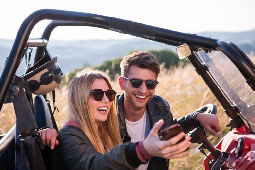 young happy excited couple enjoying beautiful sunny day taking selfie picture while driving a off road buggy car on mountain nature