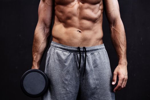 Close up of muscular bodybuilder guy doing exercises with weights over grey background. Black and white