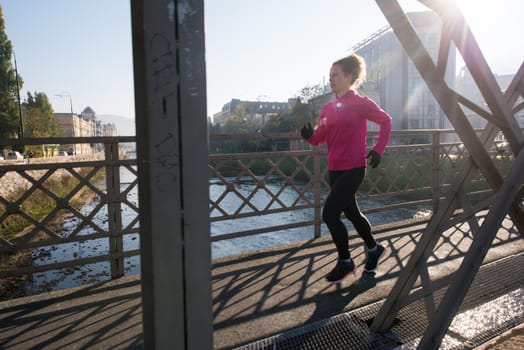 sporty woman running on sidewalk at early morning jogging with city  sunrise scene in background