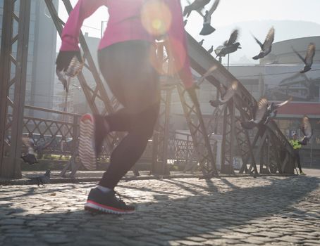 sporty woman running on sidewalk at early morning jogging with city  sunrise scene in background