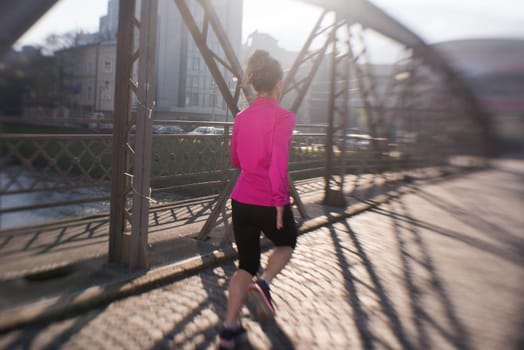 sporty woman running on sidewalk at early morning jogging with city  sunrise scene in background