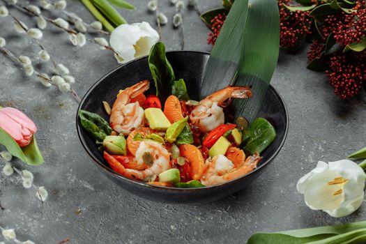 Shrimps salad with cherry tomatoes, cucumeber, avocado, lettuce and pomegranate on dish. Healthy seafood concept. Tasty grilled prawn shrimp and mix vegetable salad on black, top view.