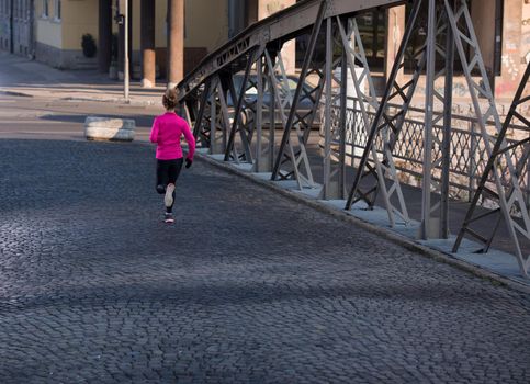 sporty woman running on sidewalk at early morning jogging with city  sunrise scene in background