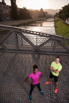 portrait of a healthy young multiethnic couple jogging in the city at early morning with sunrise in background