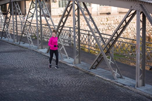 sporty woman running on sidewalk at early morning jogging with city  sunrise scene in background