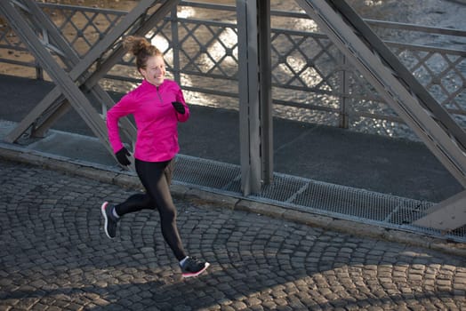 sporty woman running on sidewalk at early morning jogging with city  sunrise scene in background