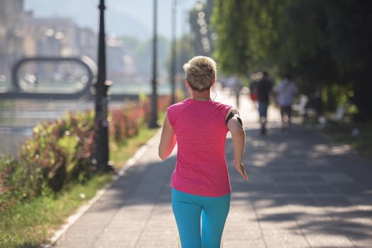 sporty woman running on sidewalk at early morning with city  sunrise scene in background