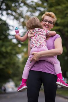 young sporty mother carries little daughter in arms while jogging in a city park,outdoor sports and fitness