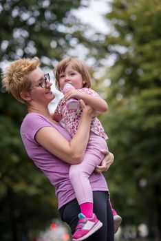 young sporty mother carries little daughter in arms while jogging in a city park,outdoor sports and fitness