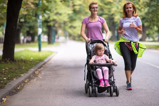 two young healthy women jogging together while pushing a baby stroller at city park