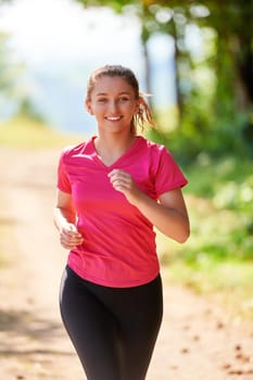 woman enjoying in a healthy lifestyle while jogging on a country road through the beautiful sunny forest, exercise and fitness concept