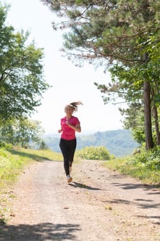 woman enjoying in a healthy lifestyle while jogging on a country road through the beautiful sunny forest, exercise and fitness concept