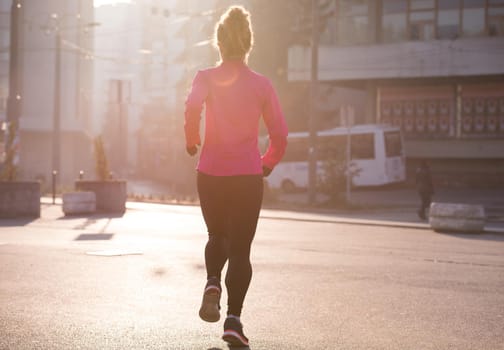 sporty woman running on sidewalk at early morning jogging with city  sunrise scene in background