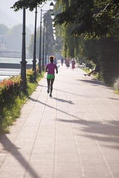 Beautiful young sporty african american woman running at early morning jogging with city sunrise scene in background