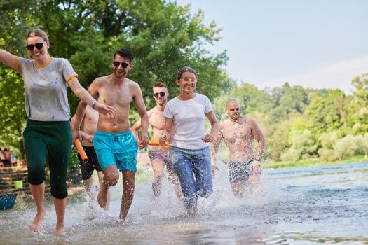 Summer joy group of happy friends having fun while running and splashing on river