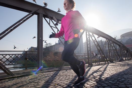 sporty woman running on sidewalk at early morning jogging with city  sunrise scene in background